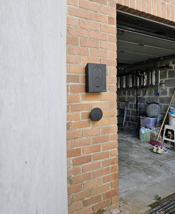 Deurbel en garageopener gemonteerd op een bakstenen muur naast een open garage.