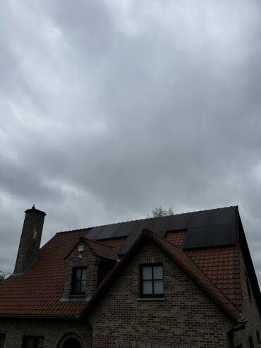 Een bakstenen huis van twee verdiepingen met een rood pannendak dat gedeeltelijk bedekt is met zonnepanelen. De lucht erboven is bewolkt.