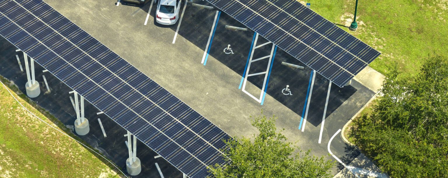 Luchtfoto van parkeerplaats met met zonnepanelen bedekte carportschuilplaatsen en aangewezen rolstoeltoegankelijke parkeerplaatsen.