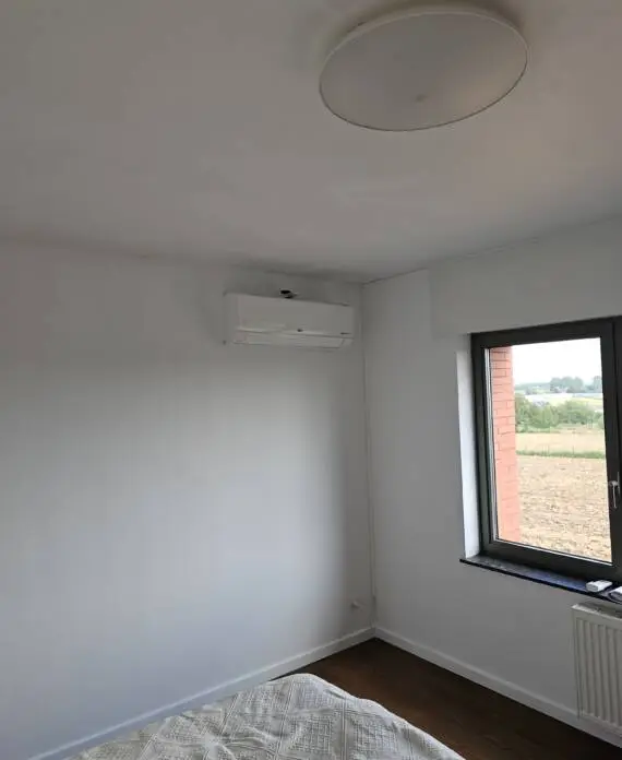 Een kamer met witte muren, een bed, een raam met uitzicht op het landschap en een efficiënt HVAC-systeem aan de muur.