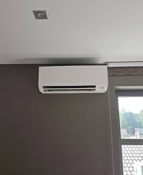 Een aan de muur gemonteerde airco-unit wordt boven een raam met een gedeeltelijk gesloten gordijn in een kamer met een donkere muur geïnstalleerd en zorgt voor een efficiënt koelsysteem.