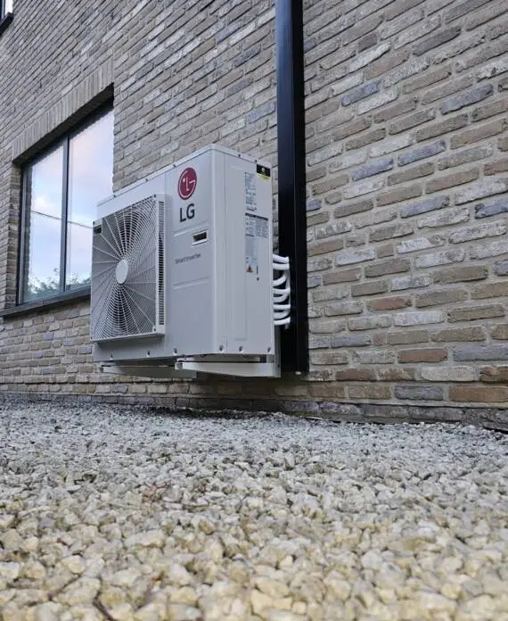 Een LG-airconditioningunit voor buiten is op een bakstenen muur boven een met grind bedekte ondergrond gemonteerd.