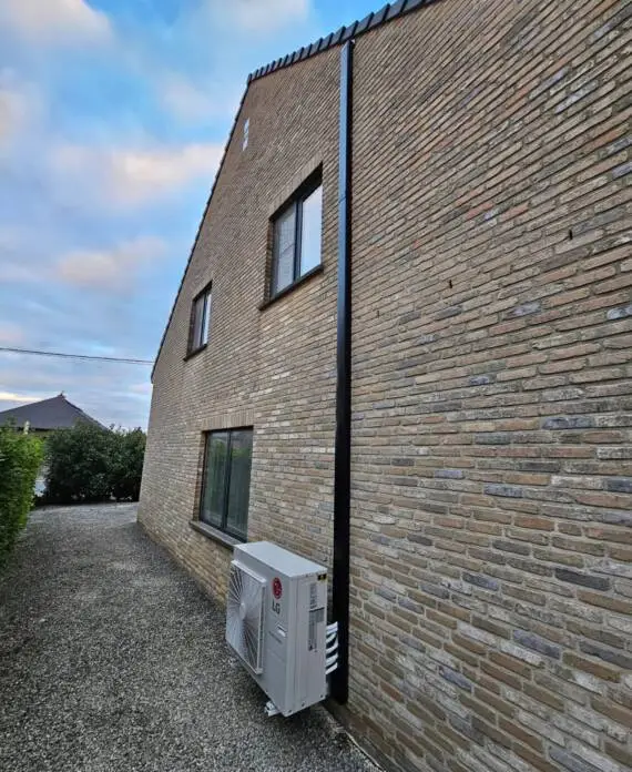 Zijaanzicht van een bakstenen gebouw met twee ramen en een airconditioningunit buiten. De lucht is gedeeltelijk bewolkt.