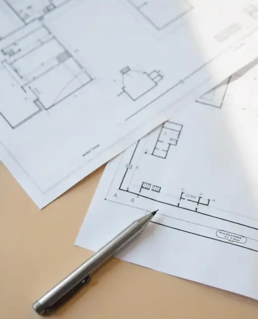 Architectonische blauwdrukken op een tafel met een zilveren pen erop. De plannen, conform de regelgeving, tonen gedetailleerde indelingen van bouwruimtes en ingewikkelde paden voor elektriciteit. Architectonische blauwdrukken op een tafel met een zilveren pen erop. De plannen, conform de regelgeving, tonen gedetailleerde indelingen van bouwruimtes en ingewikkelde paden voor elektriciteit.